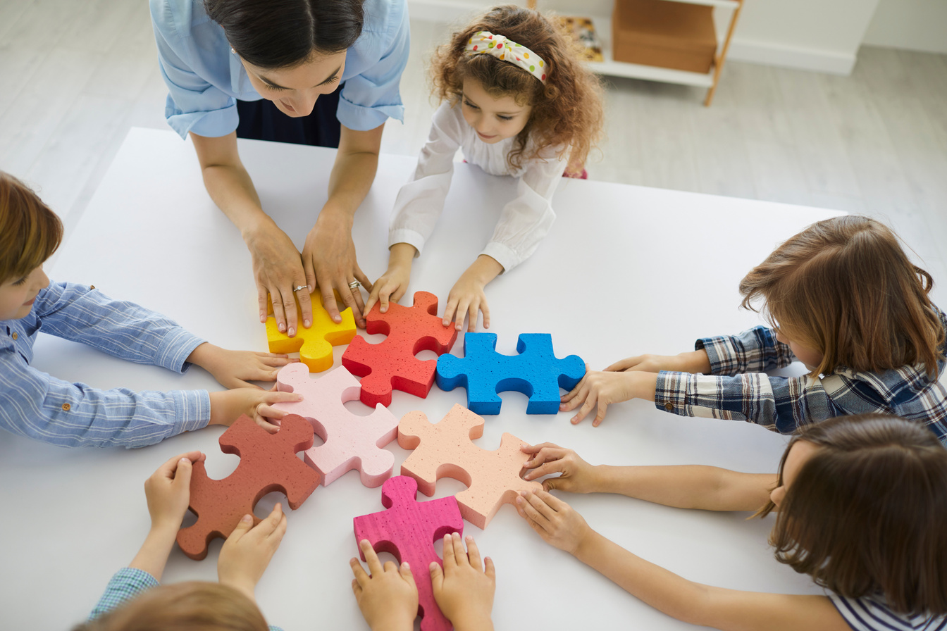 Team of Little School Children with Teacher Putting Together Pieces of Jigsaw Puzzle